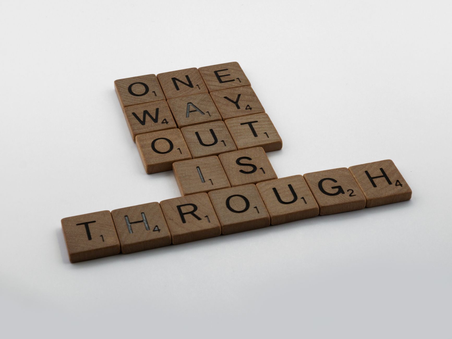 Close-up of Scrabble tiles spelling 'one way out is through' on a white surface.