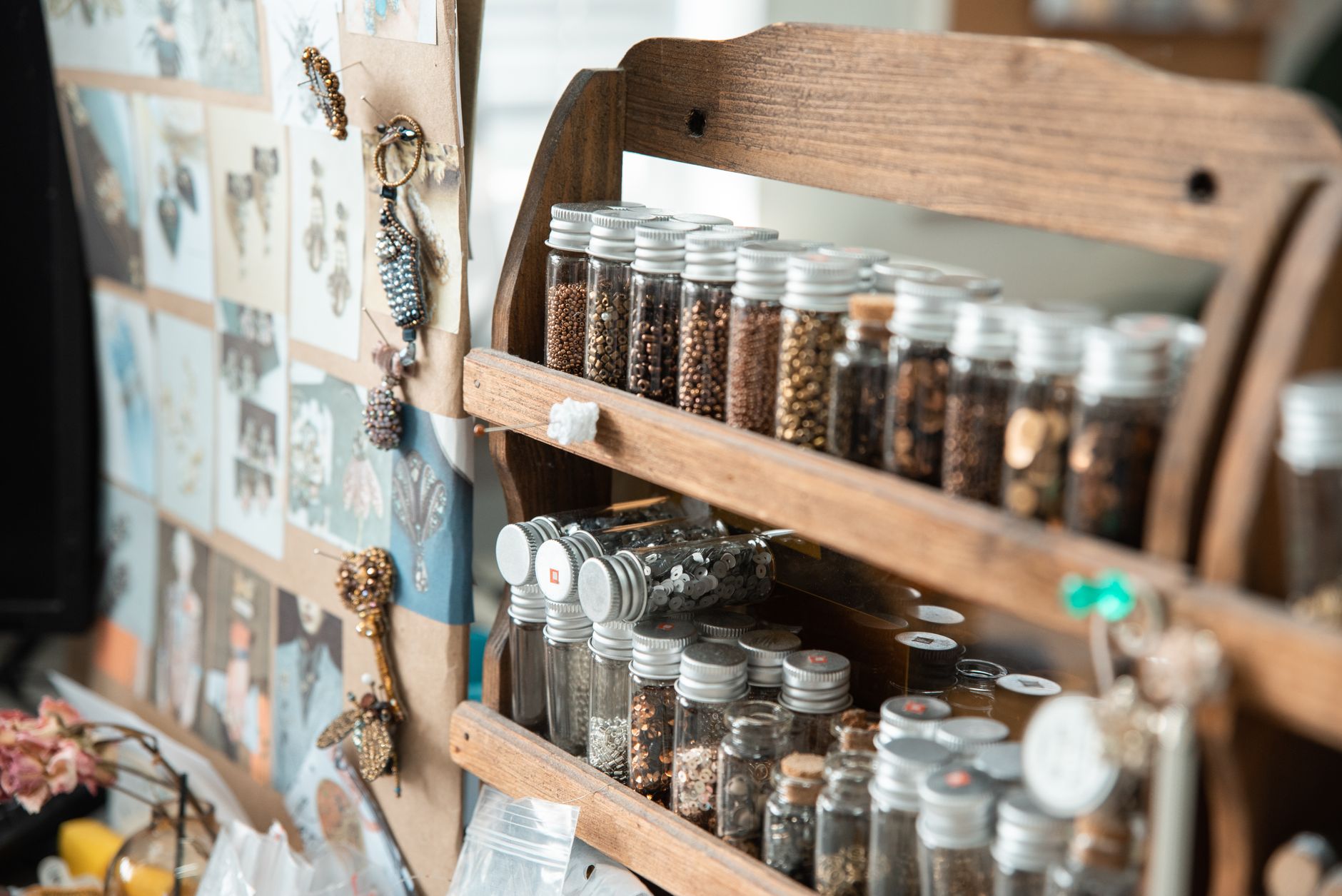 Close-up of a home sewing space with beads, a moodboard, and organized jar collection for creative projects.