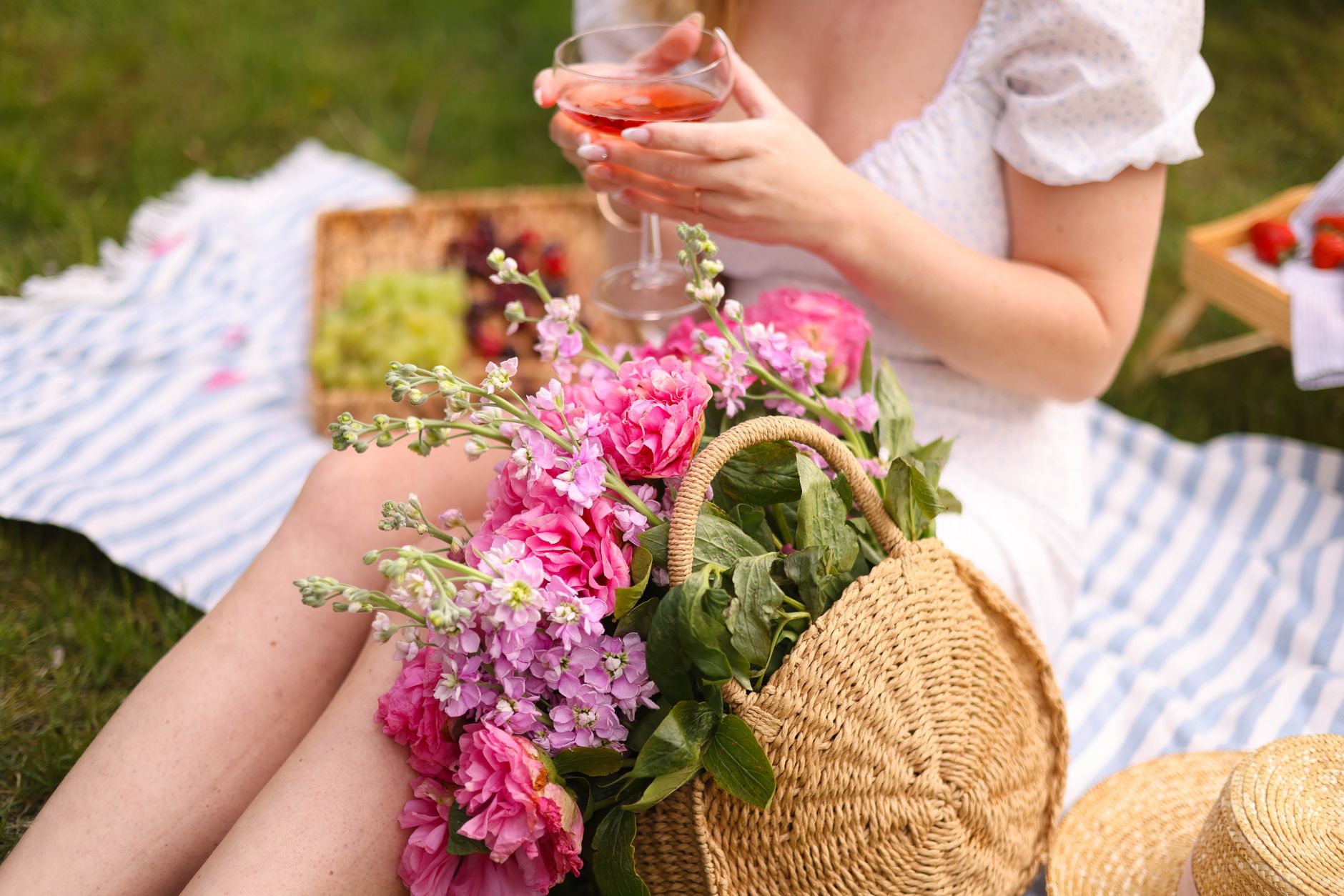 A woman enjoying a summer picnic with flowers and a refreshing drink in the park.