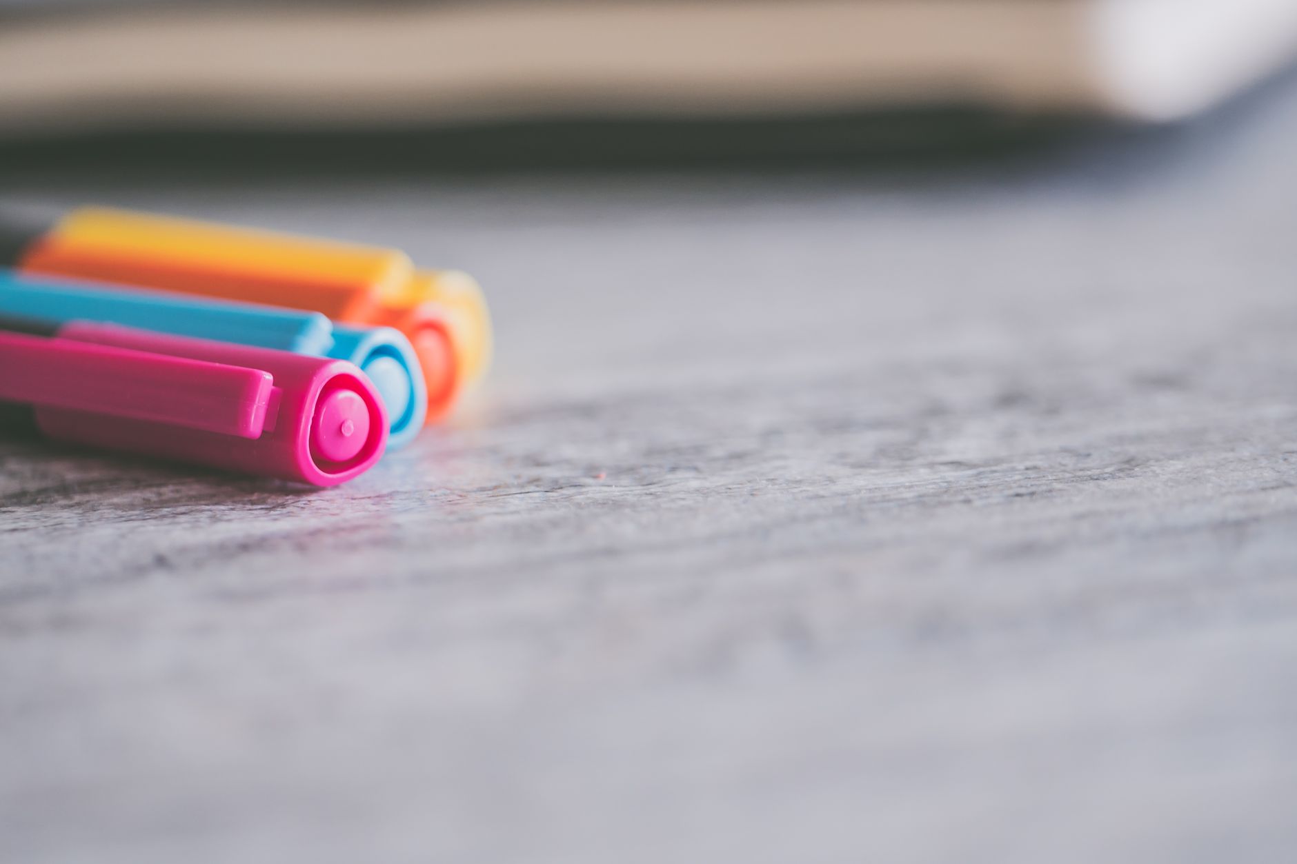 Close-up of vibrant colored pens on a textured wooden desk surface, ideal for office or art themes.